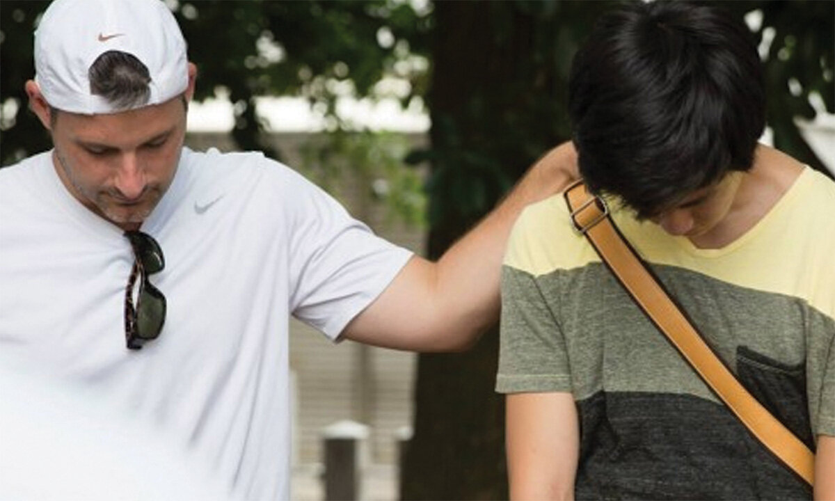 Man praying with teen outdoors, hand on shoulder.