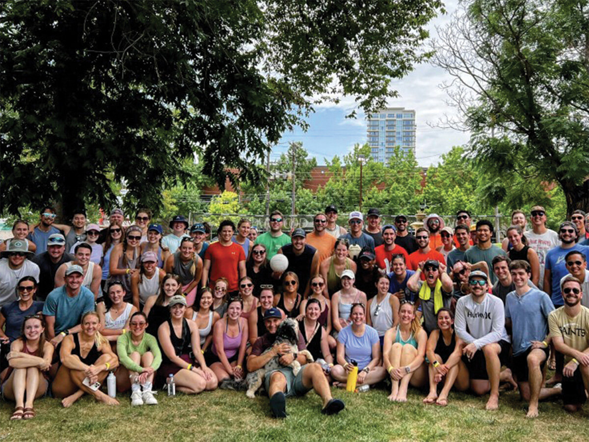 Large group of young adults gathered outdoors in a park, smiling together for a group photo.