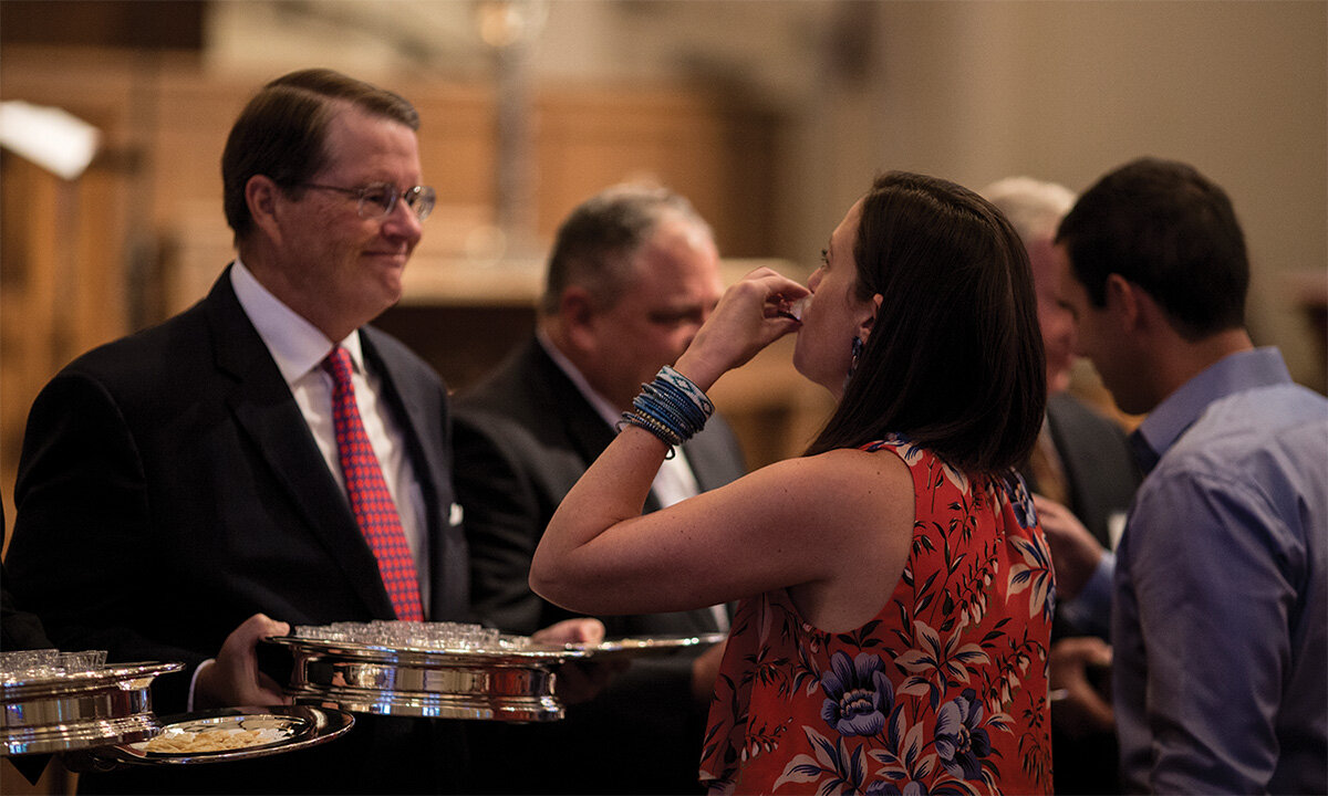 Woman receiving communion bread from a church leader holding a silver tray during a worship service.