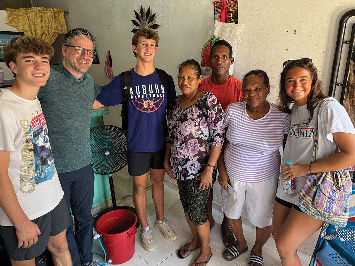 Small group of mission trip volunteers standing with a local family inside a home during a service project visit.